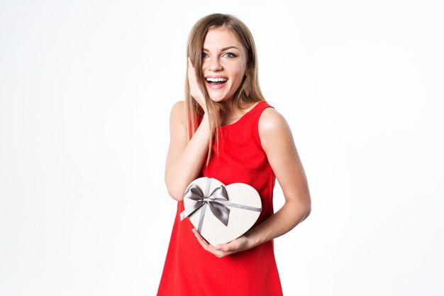 Bella donna sorpresa in un vestito rosso con un fronte di tocco del contenitore di regalo, colpo dello studio.