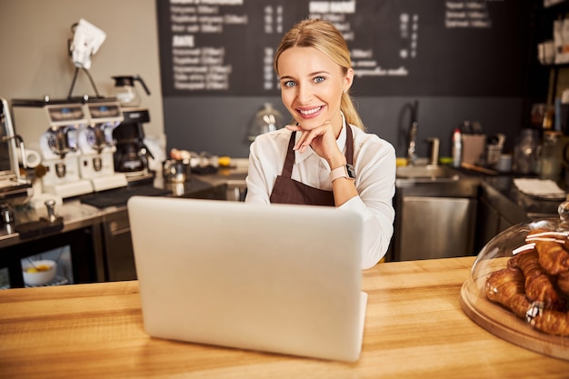 Bella donna sorridente cameriere che lavora al bar al laptop