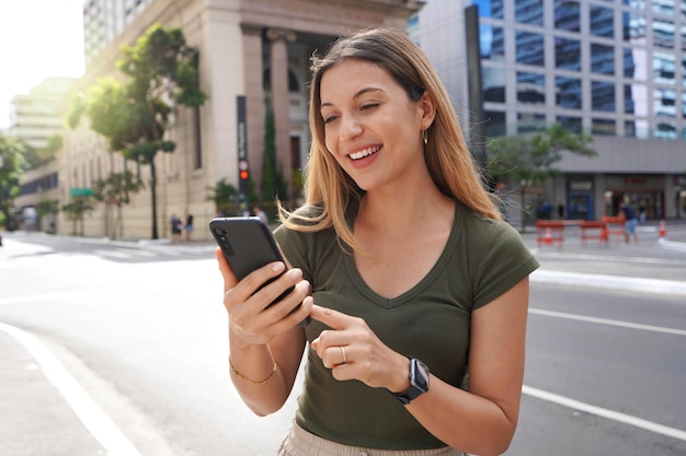 Bella donna sorridente che riceve buone notizie sullo smartphone nella metropoli moderna