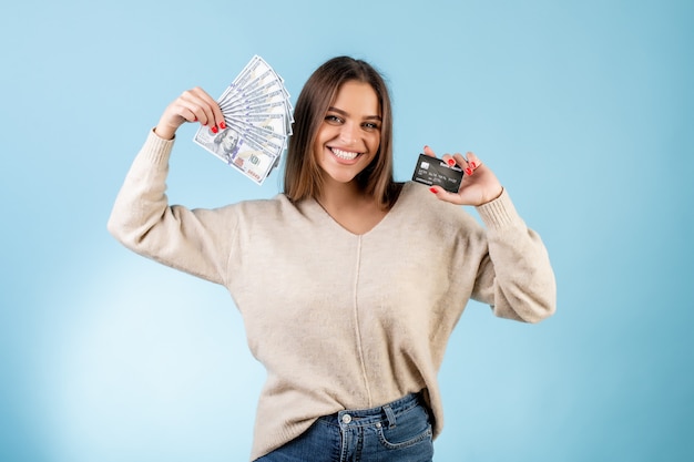 Bella donna sorridente che tiene le banconote in dollari soldi e carta di credito isolata sopra il blu