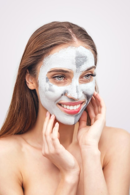 Bella donna sorridente con un'argilla o una maschera di fango sul viso su sfondo bianco