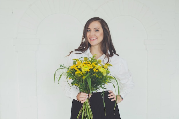 Bella donna sorridente con un bouquet di fiori gialli su sfondo bianco