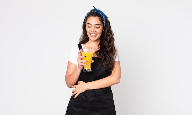 Bella donna sorridente con un'espressione felice e sicura con la mano sul mento e in possesso di un bicchiere di succo d'arancia