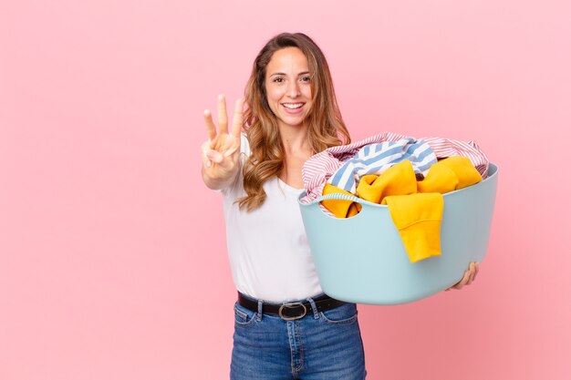 Bella donna sorridente e dall'aspetto amichevole, mostrando il numero tre e lavando i vestiti.