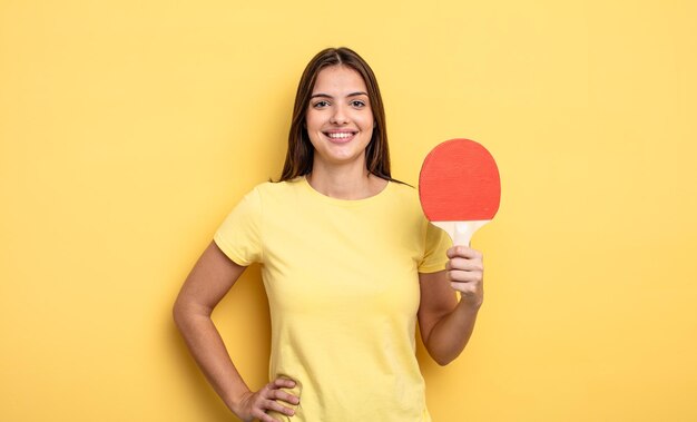 Bella donna sorridente felicemente con una mano sull'anca e fiducioso concetto di ping pong