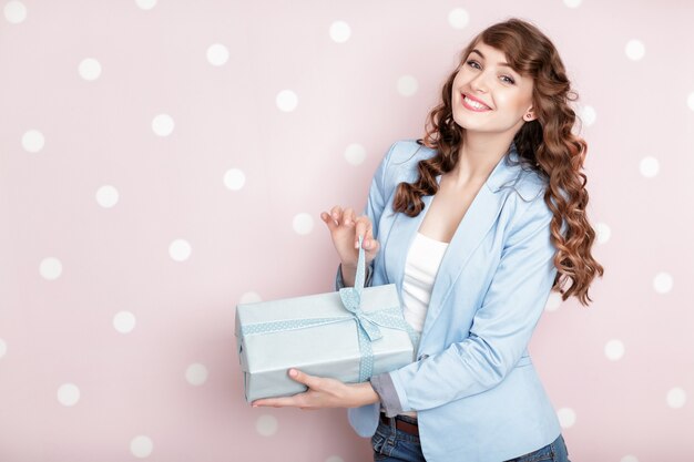 Bella donna sorridente in giacca blu tiene confezione regalo con i capelli ricci