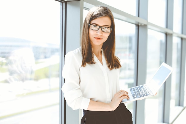 Bella donna specialista con computer portatile in piedi in un ufficio moderno e sorridente affascinante Lavorando sulla strategia del piano di analisi dei dati di progettazione Concetto di uomini d'affari