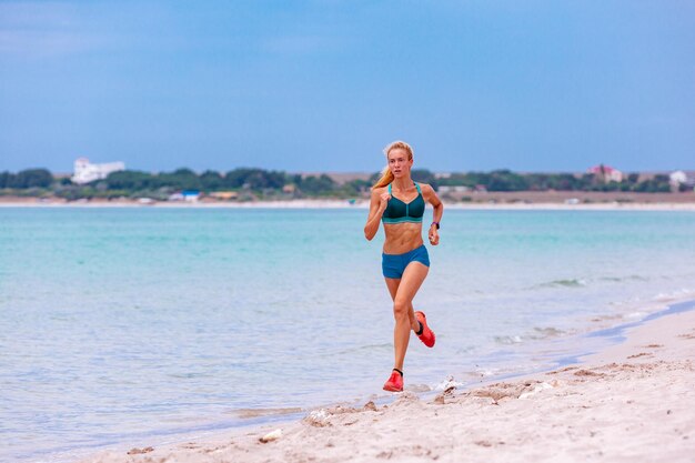 Bella donna sportiva che corre lungo uno stile di vita sano sulla bella spiaggia sabbiosa godendo le vacanze estive attive vicino al mare