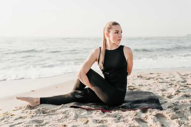 Bella donna sportiva che fa yoga sulla spiaggia vicino all'oceano