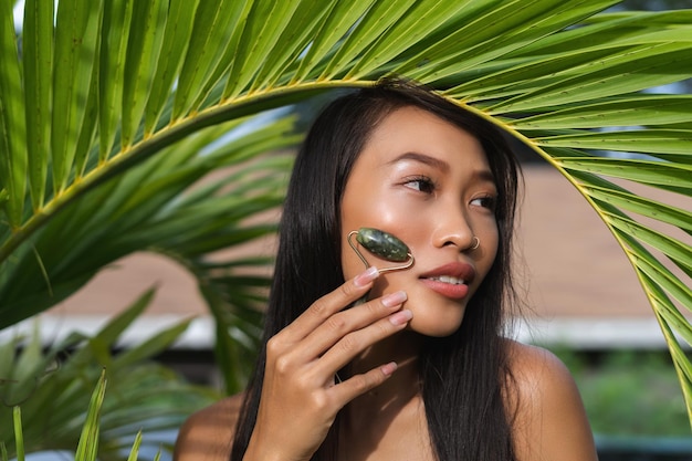 Bella donna tailandese asiatica con la pelle abbronzata scura pulita liscia morbida bellezza ritratto rullo massaggiatore cura della pelle foglie di palma all'aperto