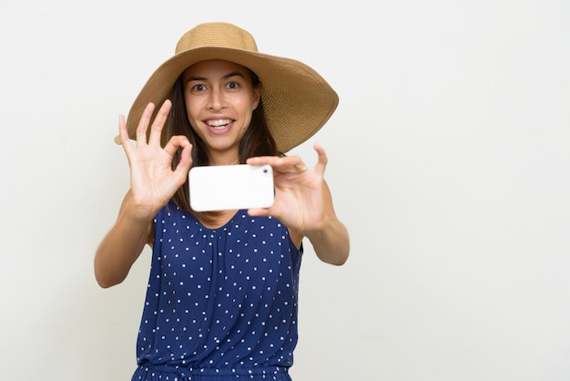 Bella donna turistica multi etnica felice che cattura maschera con il telefono e che dà segno giusto