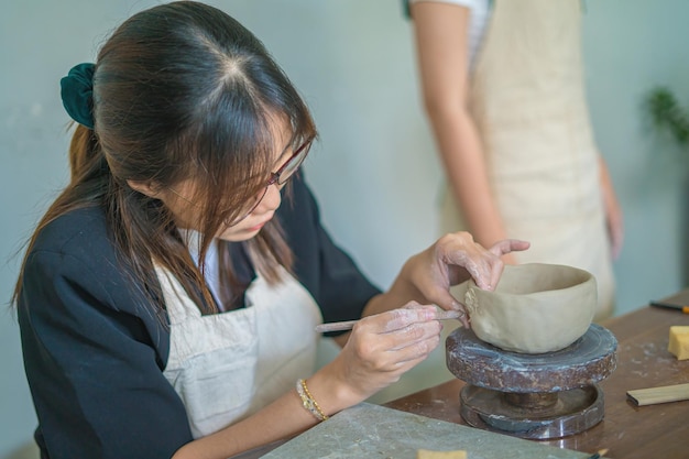 Bella donna vasaio che lavora sul tornio del vasaio che fa vaso di ceramica dall'argilla nel laboratorio di ceramica Mano di messa a fuoco giovane donna che attacca la parte del prodotto in argilla al futuro prodotto in ceramica Laboratorio di ceramica