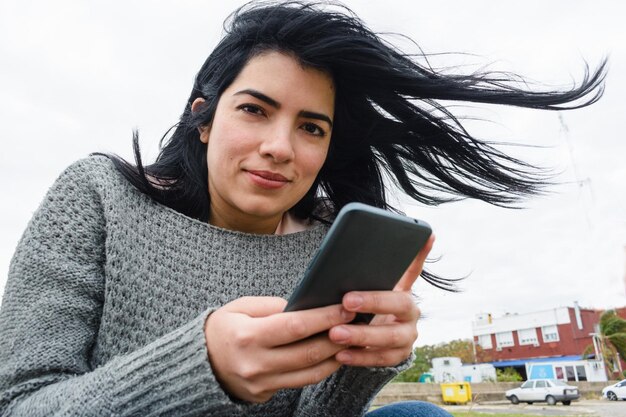 bella donna venezuelana nel patio di casa sua seduta usando il telefono guardando la telecamera