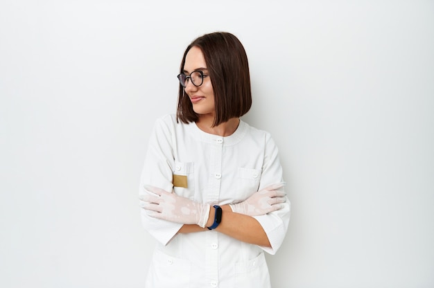 Bella dottoressa che distoglie lo sguardo mentre posa sulla macchina fotografica sopra fondo bianco con lo spazio della copia