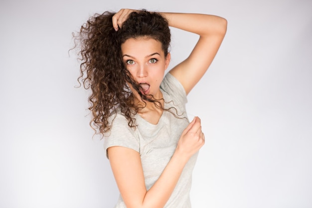 Bella e attraente giovane donna sorpresa che gioca con i capelli ricci e guardando la telecamera