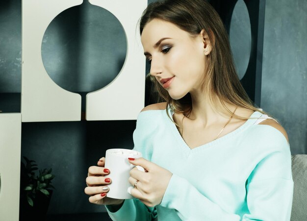 Bella e carina Bella giovane donna che tiene una tazza di caffè e si siede su una sedia a casa Concetto di stile di vita