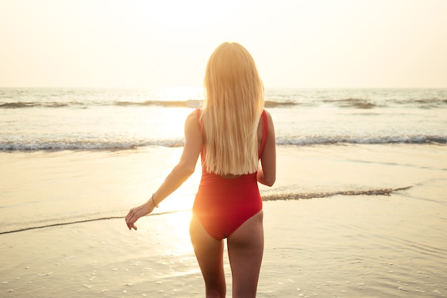 Bella e giovane donna in un costume da bagno rosso sexy corre al mare nei raggi del tramonto. tempo felice in vacanza.