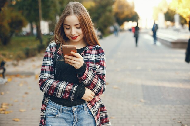 bella e luminosa ragazza che cammina intorno alla città soleggiata di primavera e usando il telefono