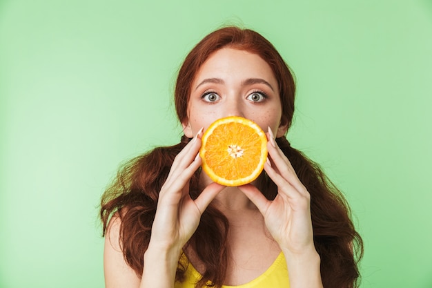 Bella eccitato giovane ragazza rossa in posa isolato su parete verde sfondo con agrumi vitamine frutti.