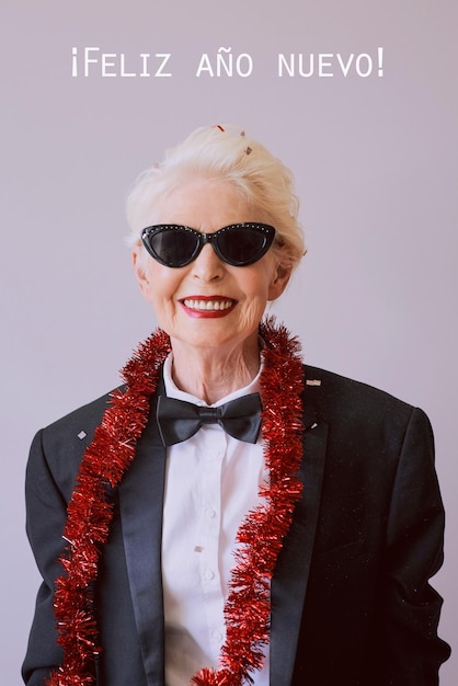 Bella ed elegante donna anziana matura con occhiali da sole e smoking che celebra il nuovo anno Fun party sty