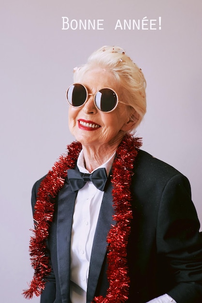 Bella ed elegante donna anziana matura con occhiali da sole e smoking che celebra il nuovo anno Fun party sty
