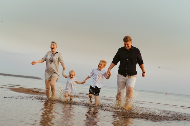 Bella famiglia caucasica che si diverte a correre in mare al tramontoVacanze estive con i bambini