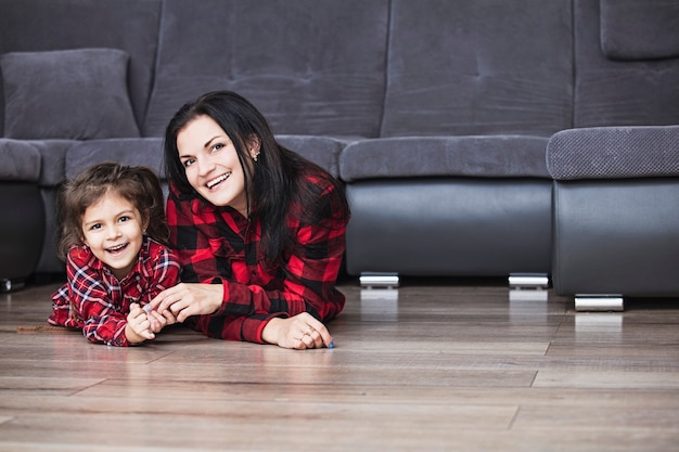 Bella famiglia felice madre e figlia che sorridono insieme a casa sdraiata sul pavimento di legno