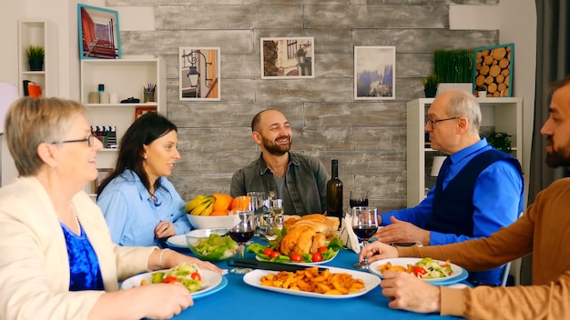 Bella famiglia multigenerazionale che cena insieme a cibo delizioso in una stanza accogliente e luminosa