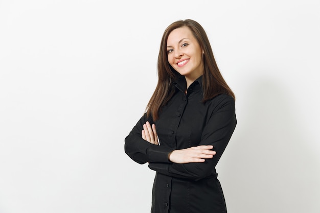 Bella felice giovane caucasica sorridente donna d'affari dai capelli castani in camicia nera classica e gonna che si tiene per mano incrociata isolata sul muro bianco