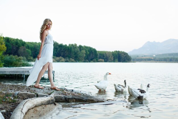 Bella femmina bionda che cammina accanto al lago circondato da anatre