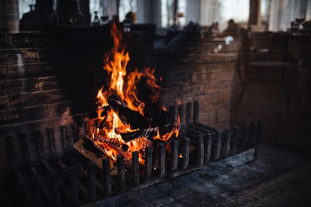 Bella fiamma di fuoco brillante Fuoco ardente sullo sfondo del muro di mattoni Colori scuri Legna ardente con fumo Grande calore Braci ardenti