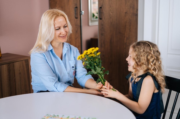 Bella figlia regala fiori bouquet per sua madre a casa in un accogliente soggiorno Concetto di vacanza in famiglia e stare insieme