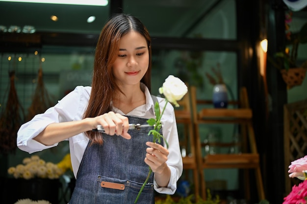 Bella fiorista asiatica che fa un bouquet che taglia un gambo di rosa con le forbici