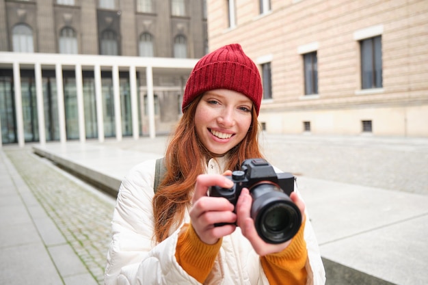 Bella fotografa ragazza readhead con fotocamera professionale scatta foto all'aperto in giro
