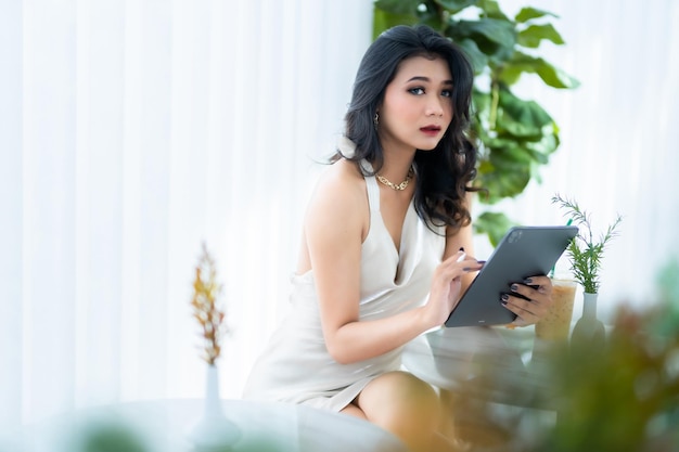 Bella freelance asiatica modello di moda donna d'affari di successo persone in abito bianco senza maniche estivo utilizzando il lavoro casual con tablet per la navigazione in internet chat e blog in caffetteria