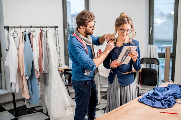 Bella giacca di misurazione del sarto sul cliente donna in piedi nello studio pieno di strumenti e attrezzature sartoriali