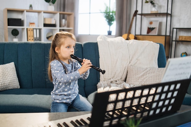 Bella giovane affascinante bambina sorridente mentre suona il flauto classico a casa