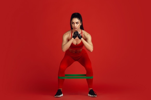 Bella giovane atleta femminile che si esercita sulla parete rossa dello studio