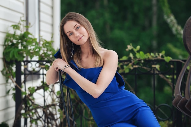 bella giovane bionda in tuta blu si siede sul balcone nella stagione calda