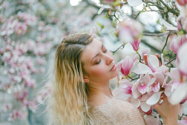 Bella giovane bionda vicino a un albero di magnolia in fiore