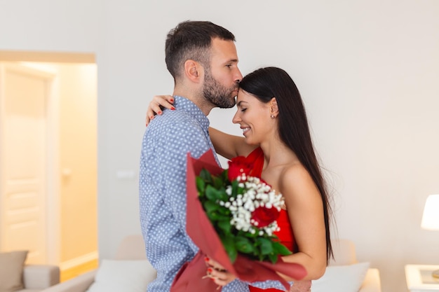 Bella giovane coppia a casa Abbracciare baciare e godersi il tempo trascorso insieme mentre si festeggia San Valentino con rose rosse