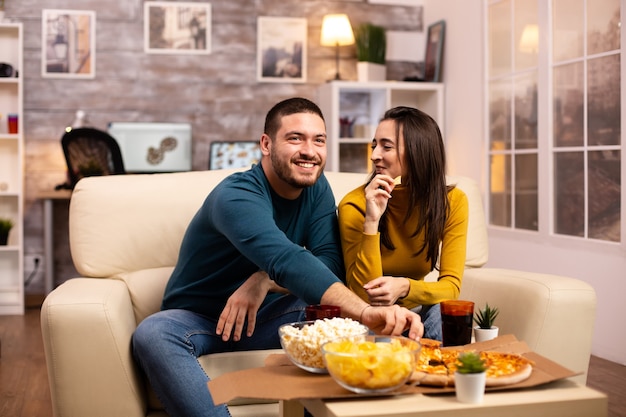 Bella giovane coppia che guarda la TV e mangia fast food da asporto in soggiorno