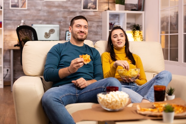 Bella giovane coppia che guarda la TV e mangia fast food da asporto in soggiorno