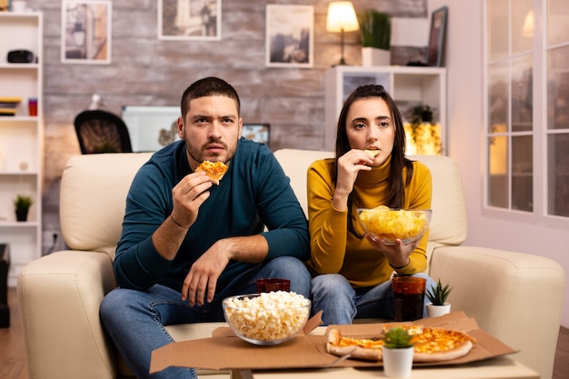 Bella giovane coppia che guarda la TV e mangia fast food da asporto in soggiorno