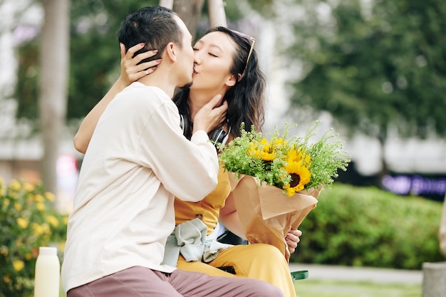 Bella giovane coppia cinese innamorata che si bacia sulla panchina nel parco quando si ha un appuntamento romantico