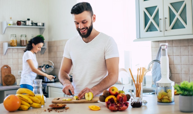 Bella giovane coppia felice emozionante nell'amore cucinare in cucina e divertirsi insieme mentre si prepara insalata di frutta fresca e sana