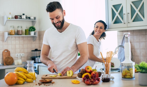 Bella giovane coppia felice emozionante nell'amore cucinare in cucina e divertirsi insieme mentre si prepara insalata di frutta fresca e sana