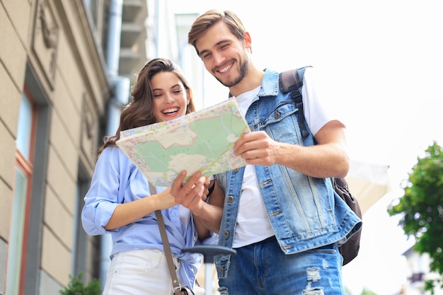 Bella giovane coppia in possesso di una mappa e sorridente mentre in piedi all'aperto.