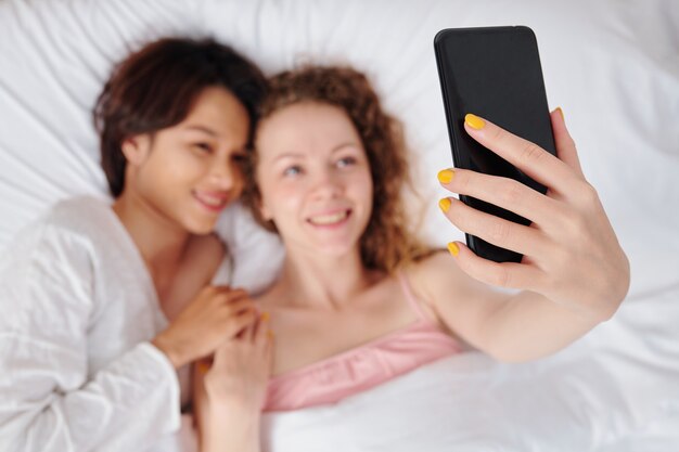 Bella giovane coppia lesbica sdraiata a letto e prendendo selfie in smartphone