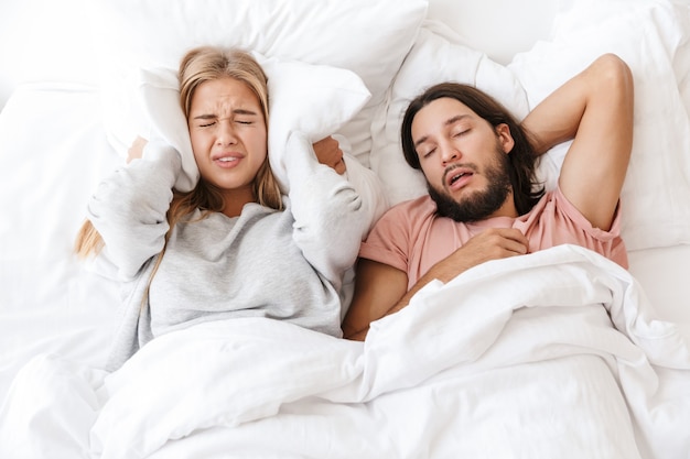Bella giovane coppia sdraiata a letto a casa, donna infastidita contro le orecchie con il cuscino